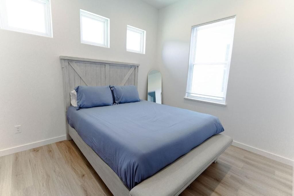 A bedroom with a bed, two windows, and a wooden floor.