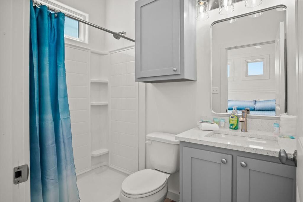 A bathroom with a white toilet, a sink with toiletries, a mirror, and a blue shower curtain.