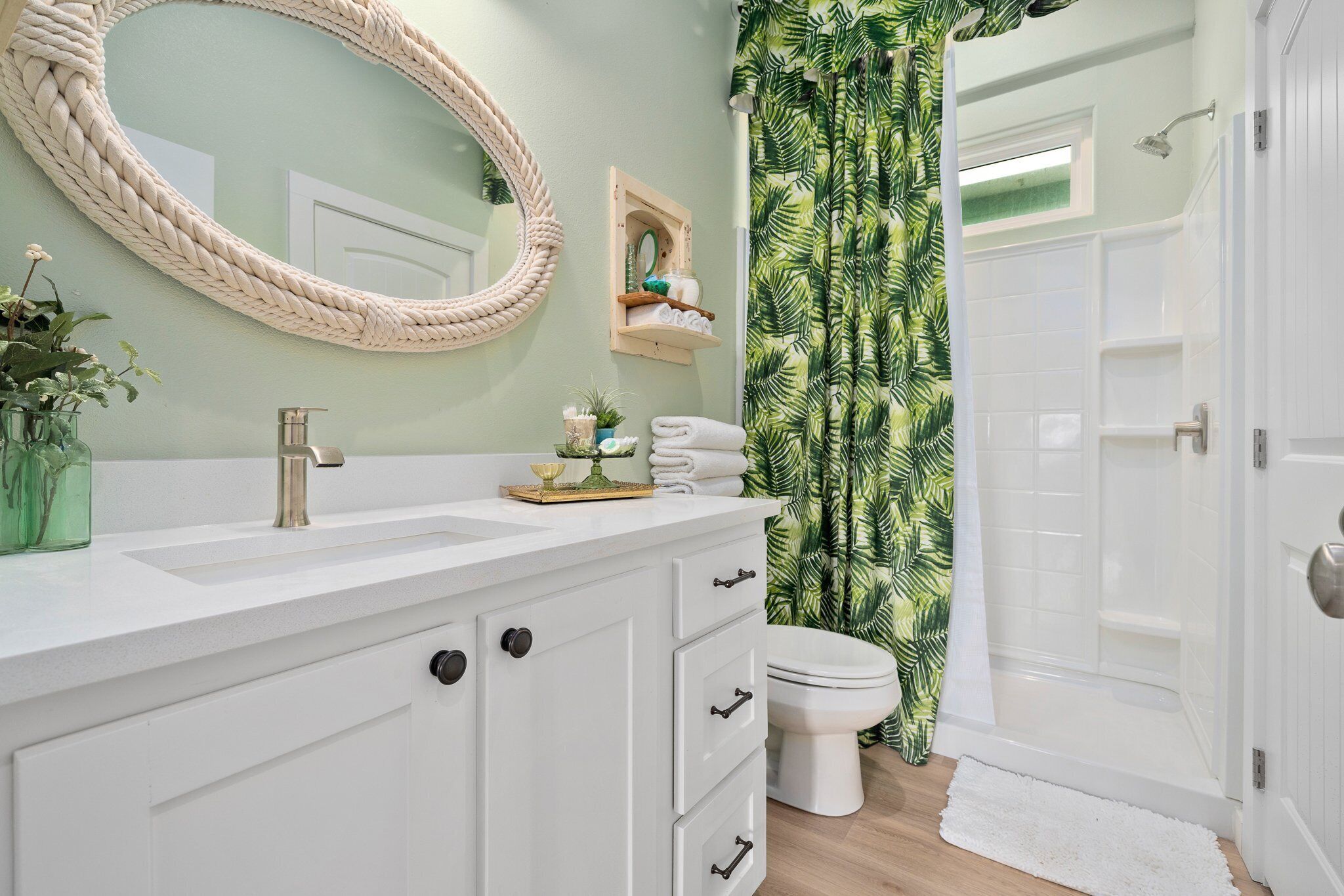 A bathroom with a white vanity, a round mirror, a toilet, and a shower area.