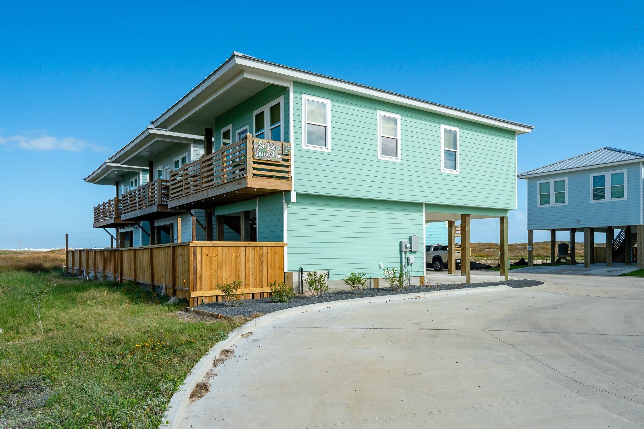 Een tweelaags huis aan het strand met een houten terras en een overdekte patio.