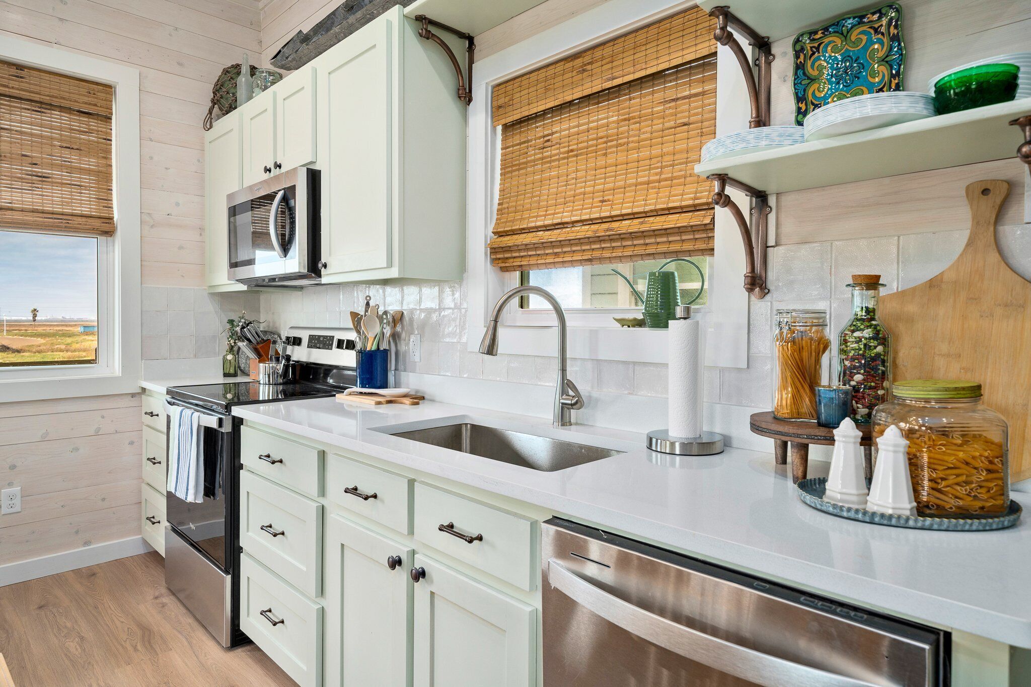 A modern kitchen with white cabinets, stainless steel appliances, and a window with a view of the countryside.