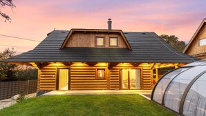 A log cabin with a sloped roof, a large glass greenhouse, and a well-maintained lawn.