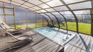 A covered outdoor hot tub area with lounge chairs and a view of a green lawn.