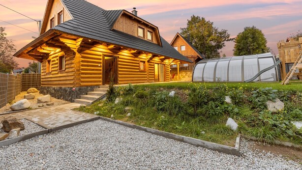 A log cabin with a steep roof, a large window, and a well-maintained garden with gravel paths and rocks.