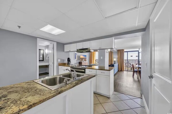 A modern kitchen with white cabinets, a granite countertop, and a stainless steel sink. - Exclusive 2-bedroom condo at Caravelle. (Myrtle Beach)