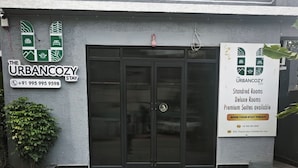 Ein Hotel Eingang mit einem Schild, das Urbancozy Stay bewirbt, einschließlich Kontaktdaten und Zimmerarten.