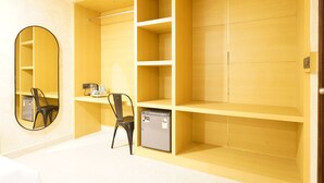 Ein Zimmer mit gelbem Wandschrank, kleinem Kühlschrank, Stuhl und Spiegel.
