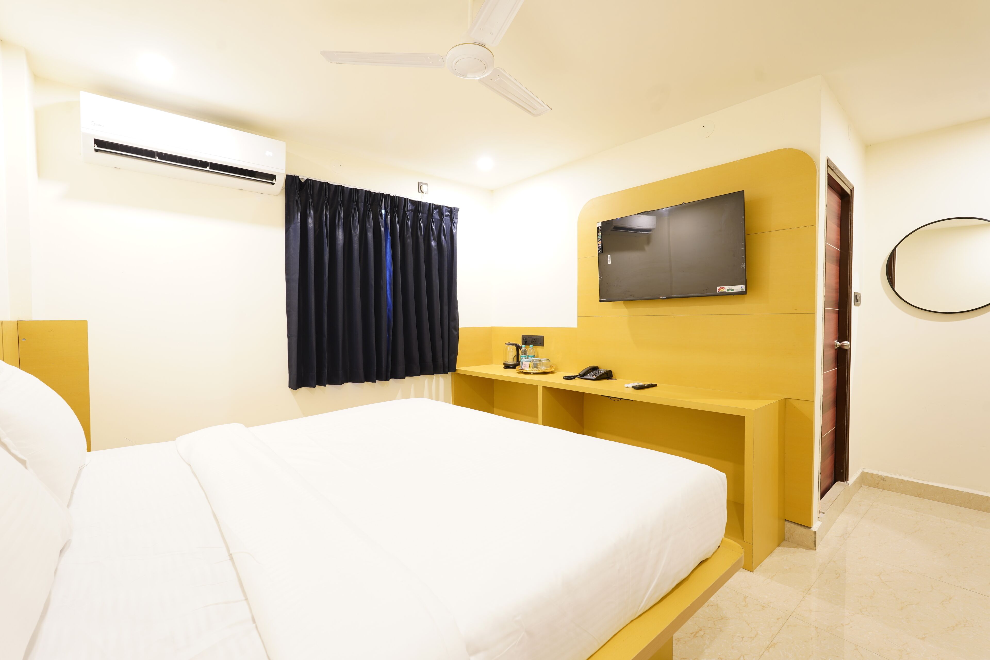 A hotel room with a bed, a desk, a television, an air conditioning unit, and a ceiling fan.