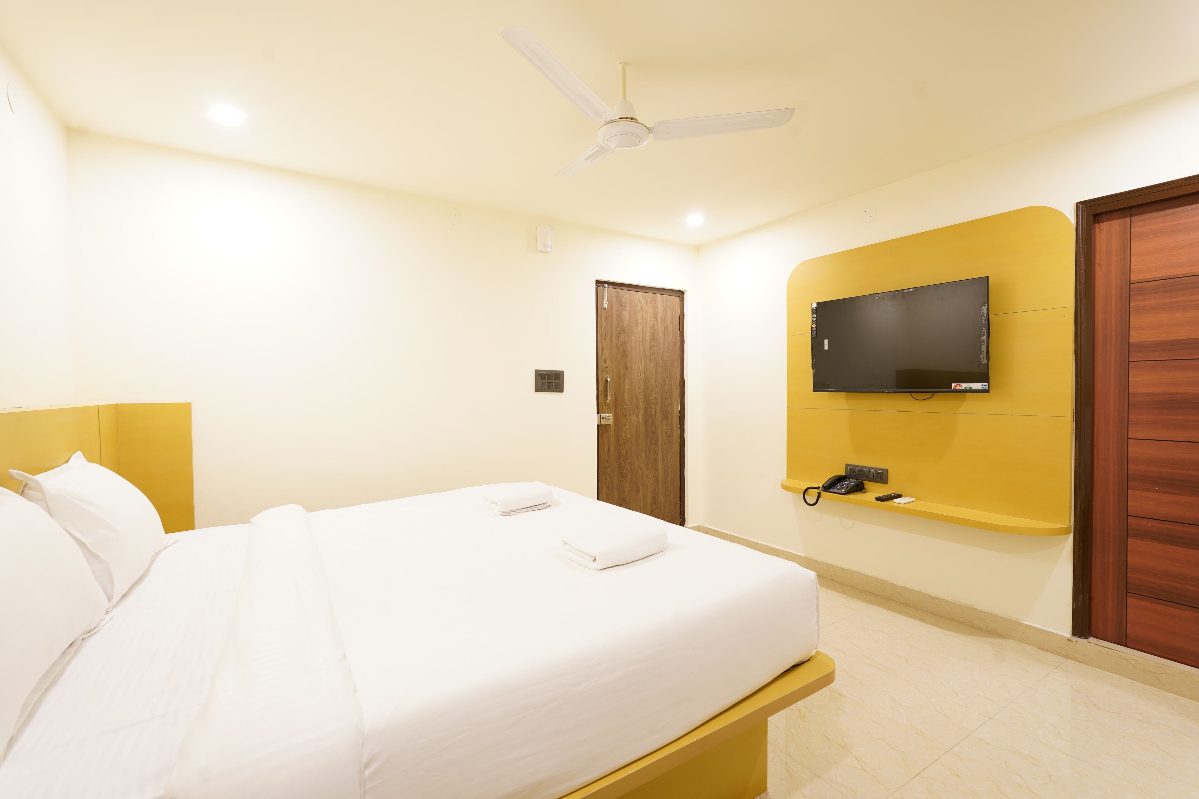 Ein Hotelzimmer mit einem Bett, einem Deckenventilator, einem an der Wand befestigten Fernseher und einer Holztür.
