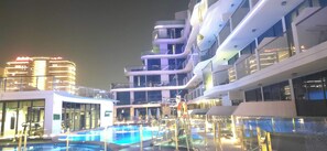 Ein modernes Hotel mit Poolbereich, mehreren Balkonen und Blick auf die nächtliche Skyline der Stadt.