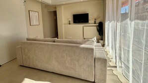 Ein Wohnzimmer mit einer Couch, einem Fernseher und einem Fenster mit durchsichtigen Vorhängen.