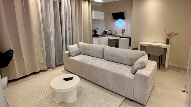 Ein modernes Wohnzimmer mit einer Couch, einem Couchtisch und einer Küchenzeile im Hintergrund.