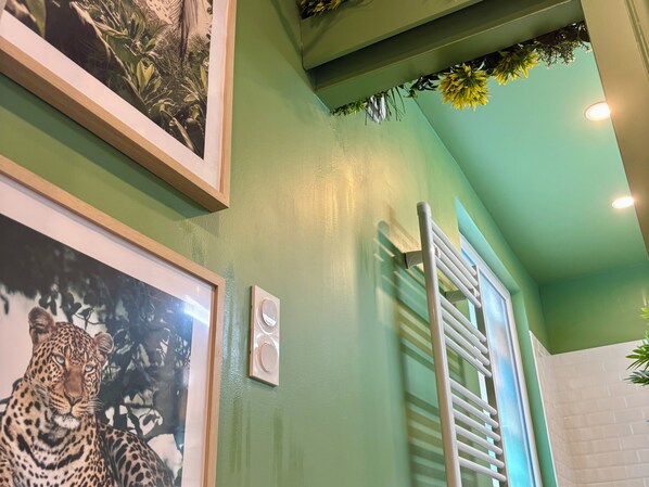 Une pièce aux murs verts, avec un radiateur et des tableaux représentant un léopard et des feuillages.