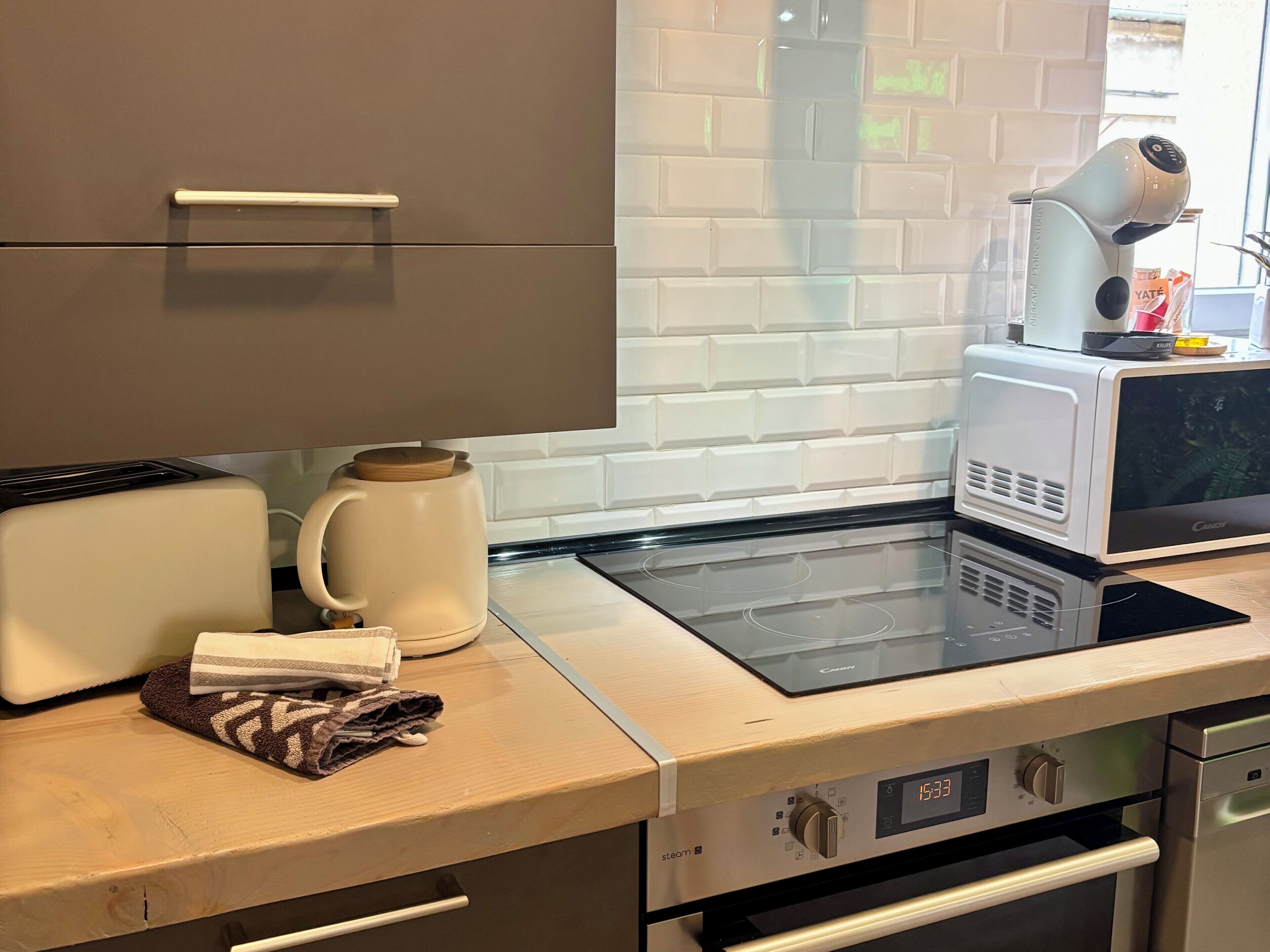 A kitchen with a microwave, toaster, kettle, and a digital clock displaying 15:33.