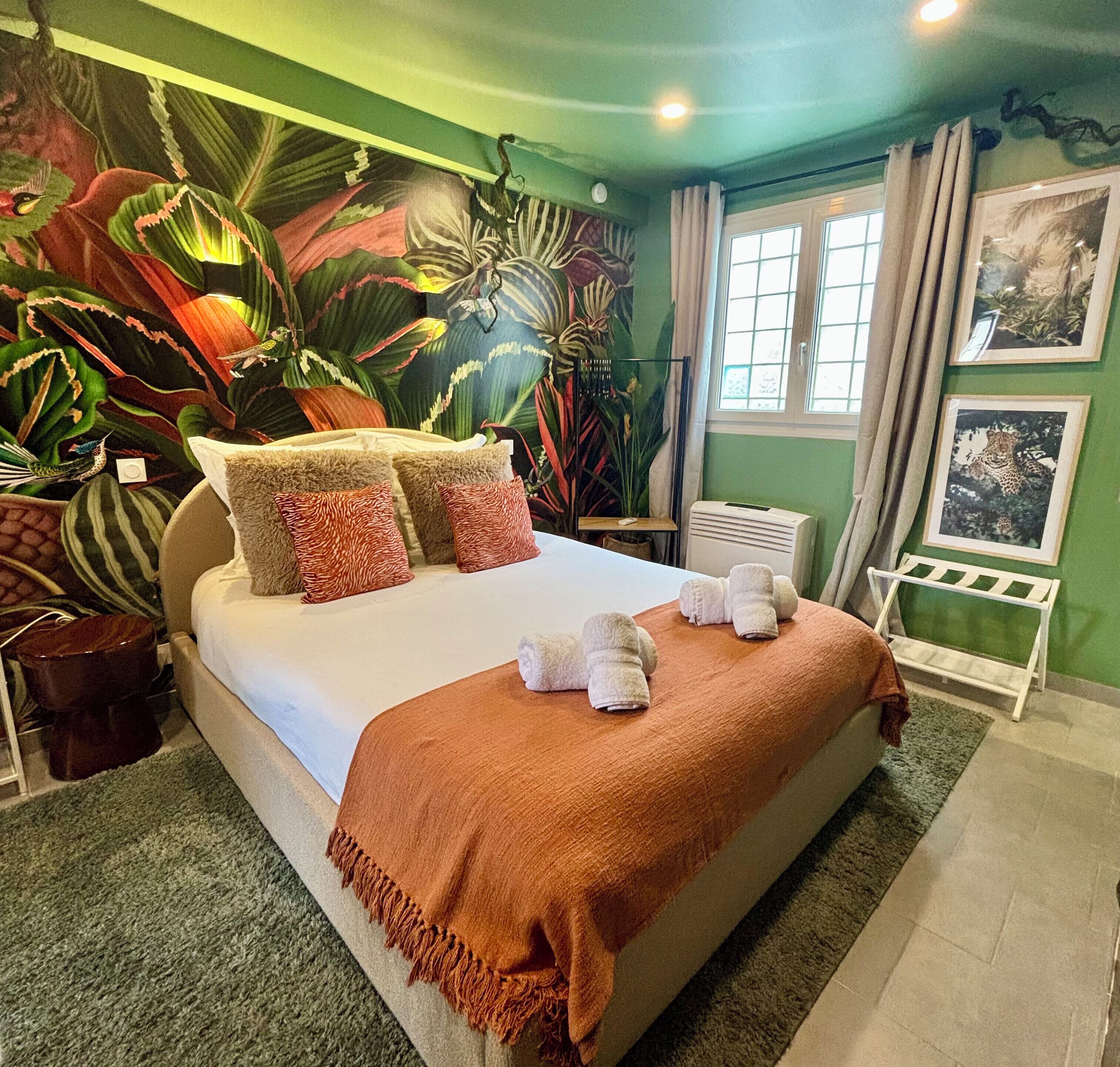 Een slaapkamer met een groot bed, groene wanden en behang met een tropisch thema.