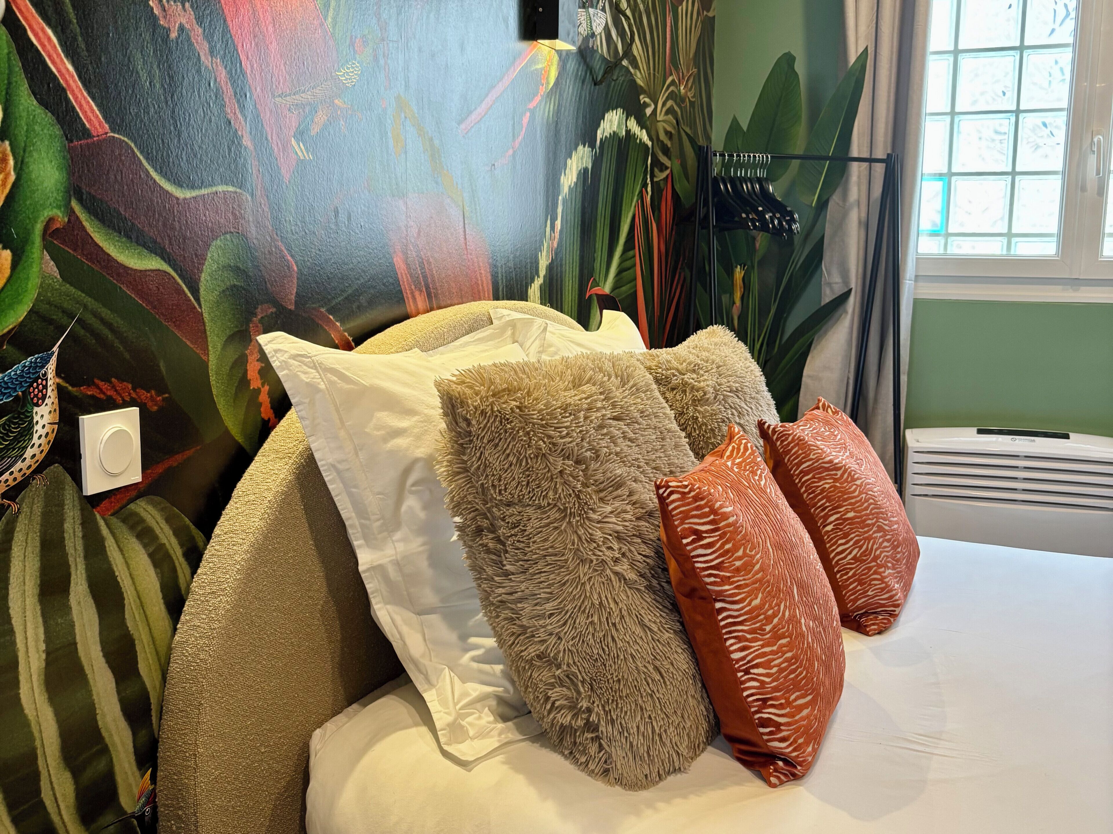 Een slaapkamer met een bed, meerdere kussens, een muurschildering en een raam.
