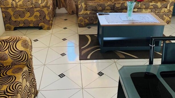 Ein Wohnzimmer mit gemusterten Sofas, einem Couchtisch mit Blumenvase und einem Fliesenboden.