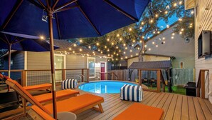 A pool area with lounge chairs and umbrellas, surrounded by string lights. - The Backyard Bliss - 4BR Heated Pool & Ping Pong (Austin)
