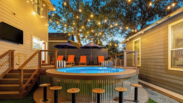 A hot tub with a wooden deck, surrounded by orange chairs and a bar area with stools. - The Backyard Bliss - 4BR Heated Pool & Ping Pong (Austin)
