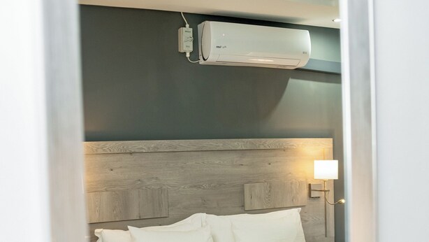 A neatly made bed with white linens and a grey accent, a bedside lamp, and a wall-mounted air conditioner. - Khayalami Hotel Secunda (Secunda)