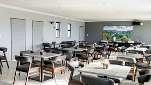 A spacious dining area with multiple tables and chairs, a large painting on the wall, and a door on the left. - Khayalami Hotel Secunda (Secunda)
