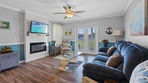 Una sala de estar con televisión, ventilador de techo, chimenea, sofá y vistas a través de puertas de vidrio.