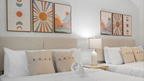 A hotel room with two beds, a nightstand with a lamp, and wall art depicting suns and landscapes. - Spacious 2BR prime location | Free Parking & Crib (Tampa)