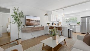 A modern living room with a flat-screen TV, wooden furniture, and a dining area with bar stools. - Spacious 2BR prime location | Free Parking & Crib (Tampa)