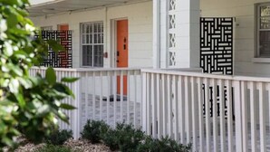 A white building with a covered porch, a red door, and decorative black lattice panels. - Spacious 2BR prime location | Free Parking & Crib (Tampa)