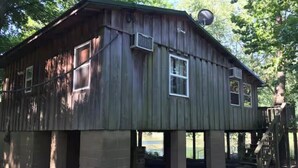 A rustic wooden cabin with a satellite dish, large windows, and a staircase leading to an upper level.
