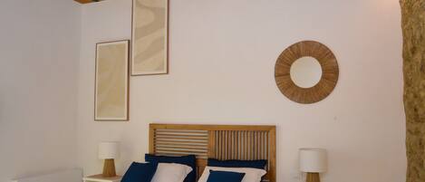 A bedroom with a wooden headboard, two bedside tables with lamps, a bed with blue and white bedding, and a circular wall decoration.