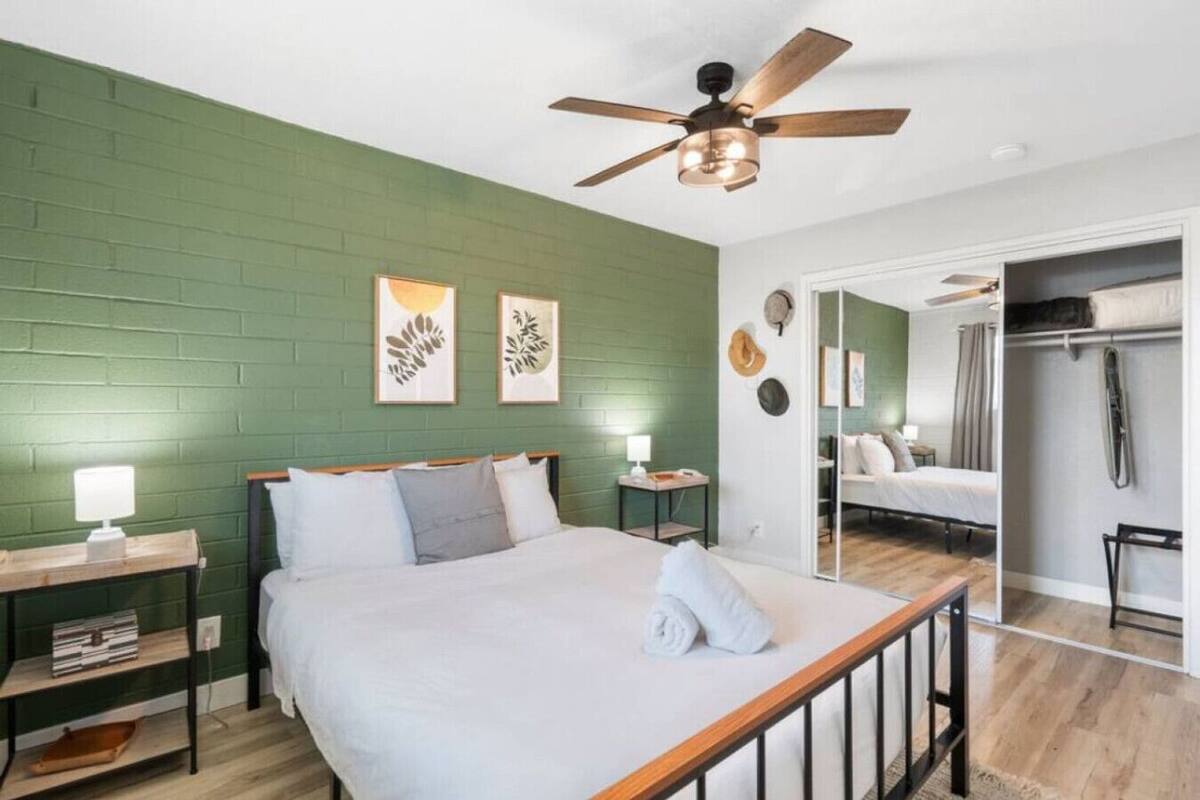 A bedroom with a bed, a nightstand, a desk, a ceiling fan, and a mirror.