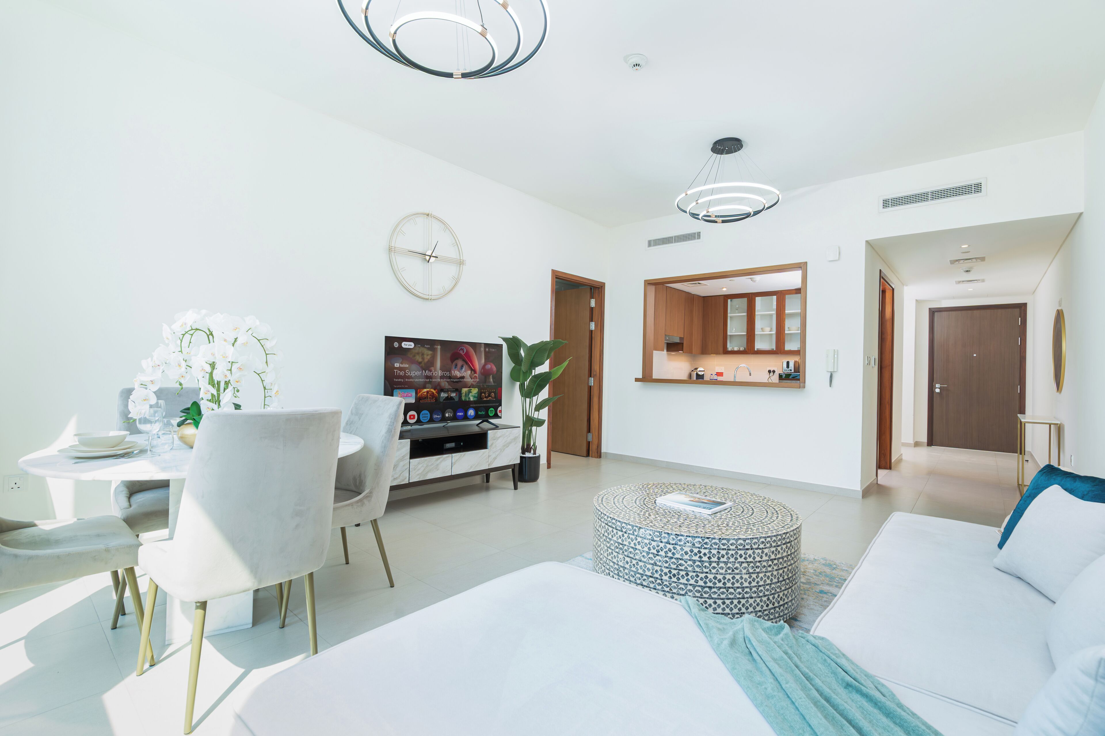 Ein modernes Hotelzimmer mit einem großen Bett, einem Essbereich mit Tisch und Stühlen, einem Fernseher und einer kleinen Küche.