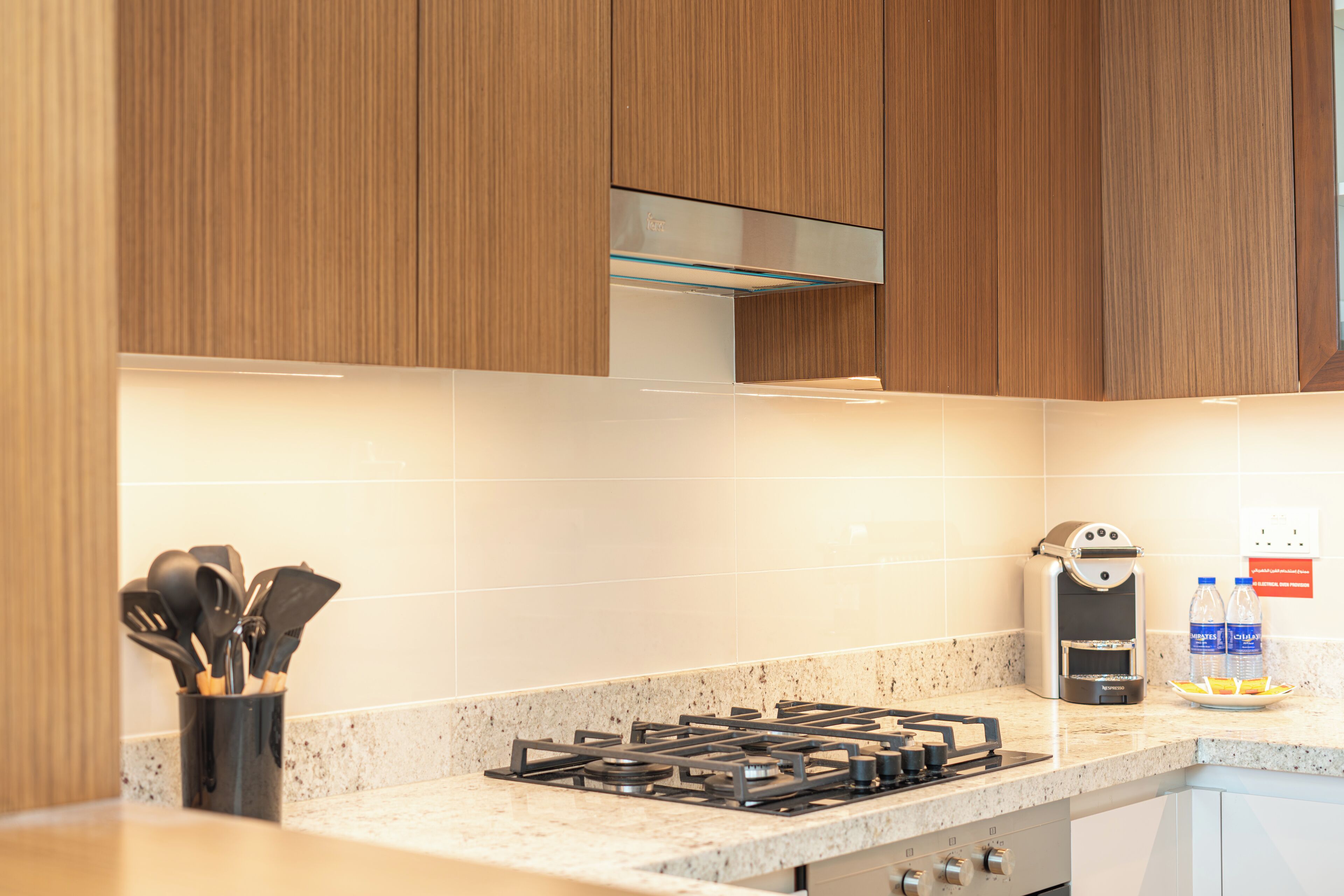 A modern kitchen with wooden cabinets, a gas stove, and a coffee machine.