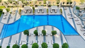 A large swimming pool with multiple sun loungers and small trees around it.