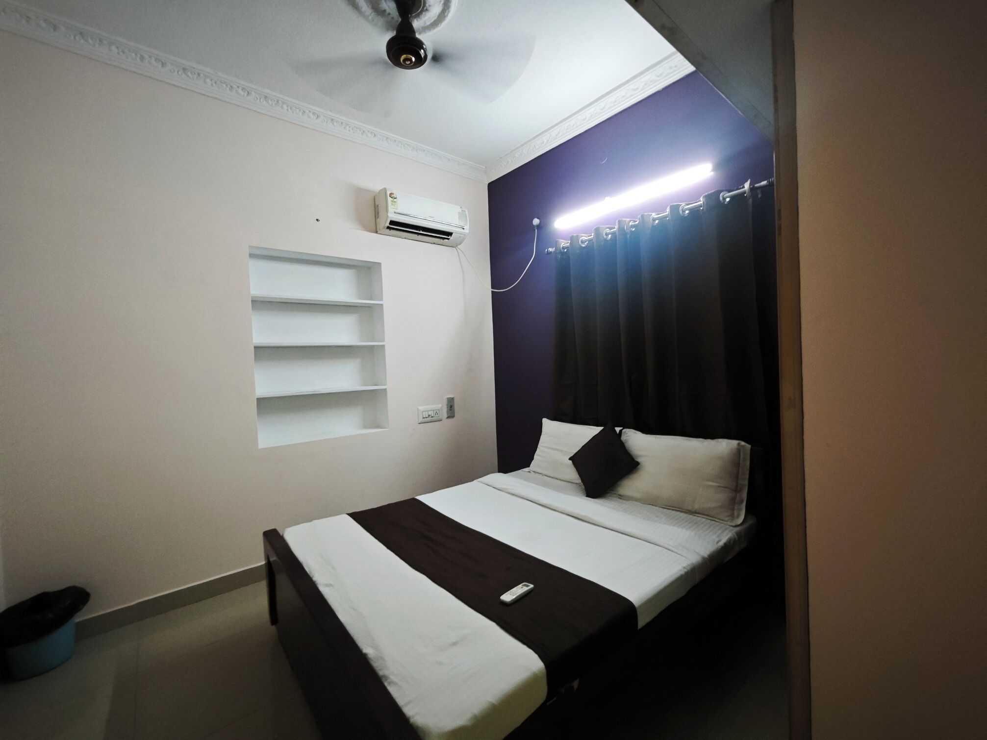 A bedroom with a bed, an air conditioning unit, a shelf, and a ceiling fan.