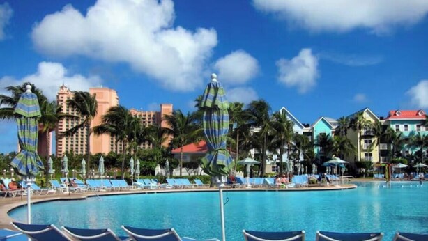 Ein Poolbereich eines Resorts mit Liegestühlen, Palmen und Hotelgebäuden im Hintergrund.