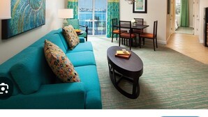 Ein Wohnzimmer mit einem türkisfarbenen Sofa, einem Esstisch mit Stühlen, einem kleinen runden Tisch und Blick durch eine Schiebetür.
