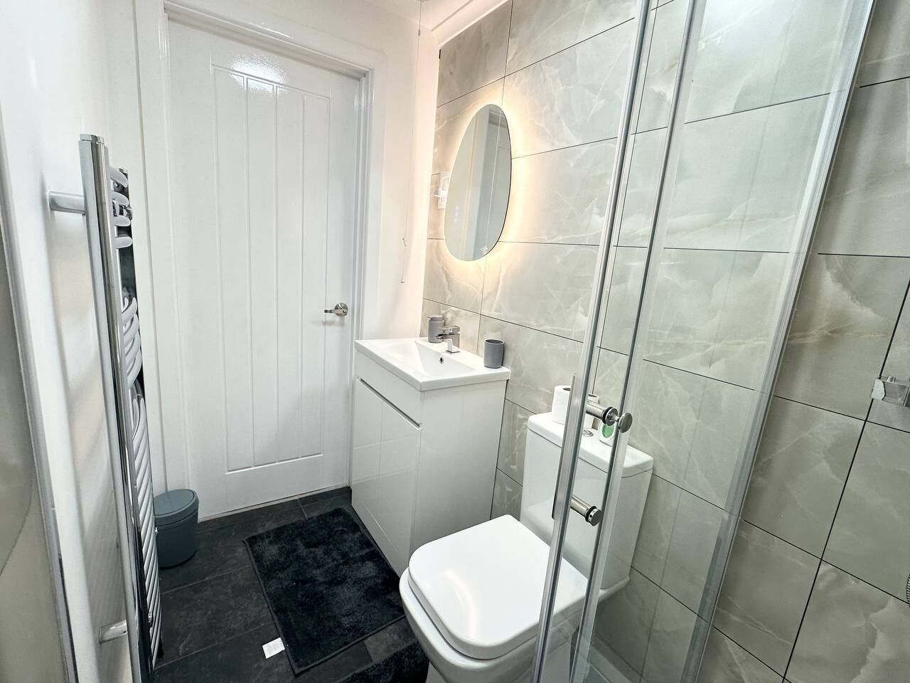 Een kleine badkamer met een wit toilet, een klein wastafeltje en een douchecabine van glas.