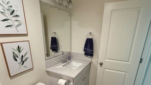 A bathroom with a toilet, sink, mirror, and two framed pictures on the wall. - New-construction, Pet-Friendly 2-bedroom house in Hanford (Hanford)