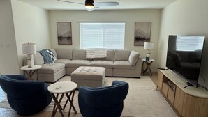 A living room with a sectional sofa, two blue armchairs, a coffee table, a TV, and artwork on the walls. - New-construction, Pet-Friendly 2-bedroom house in Hanford (Hanford)