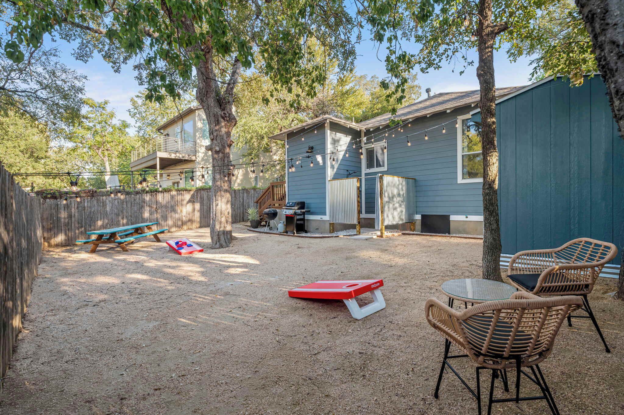 A backyard with a picnic table, two wicker chairs, a red bench, and a small table.