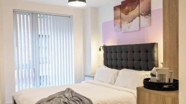 A bedroom with a bed, a nightstand, a lamp, and a window with blinds.
