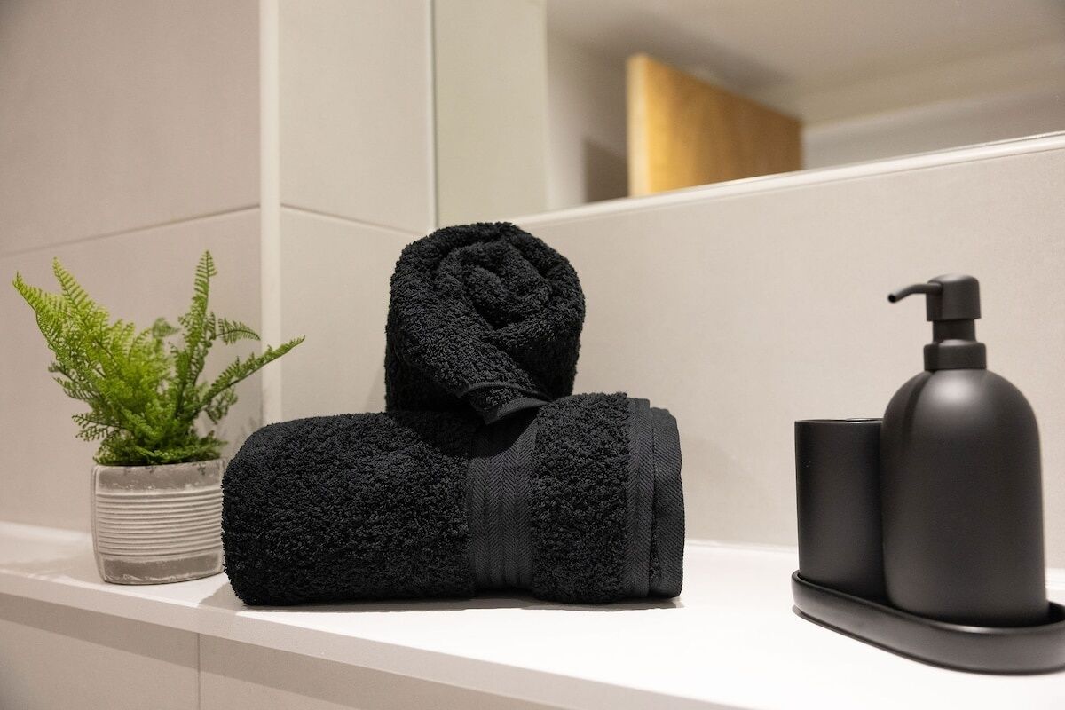 Un baño con toalla, dispensador de jabón y planta en maceta.