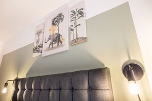 Quarto com cabeceira estofada, obra de arte na parede retratando elefantes e folhagem, e duas luminárias de parede.