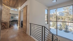 En modern inredning med ett träpanelat tak, en trappa med metallräcken och stora fönster som erbjuder en utsikt över snötäckta träd och berg.