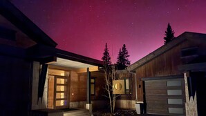 Ett modernt hus i nattens mörker, med en stjärnklar himmel, ett garage och en träfasad.
