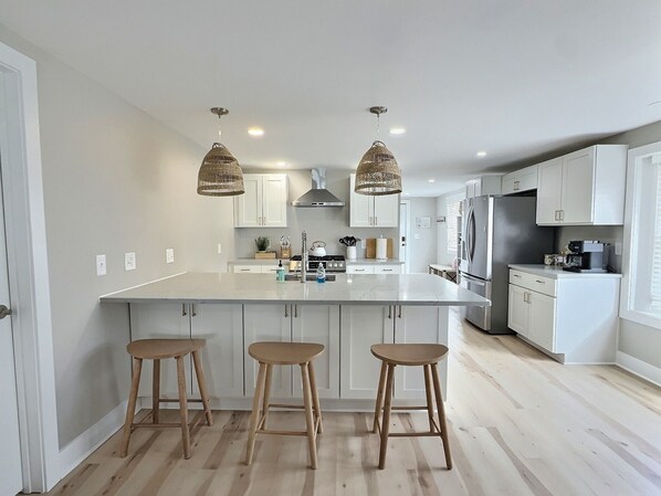 A modern kitchen with a large island, white cabinetry, and three wooden stools.