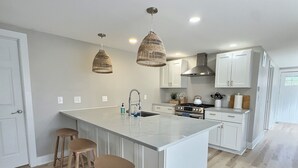 Una cocina moderna con una isla grande, armarios blancos, una estufa a gas e iluminación colgante.