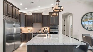 A modern kitchen with dark wood cabinets, stainless steel appliances, a marble island, and a large wall clock. - Pool & Spa | 70ft RV Garage | Near Riviera Marina (Lake Havasu City)